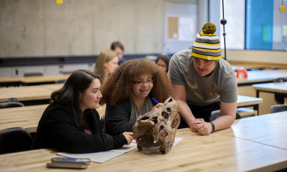 Three students in a classroom looking at an archaeological artifact